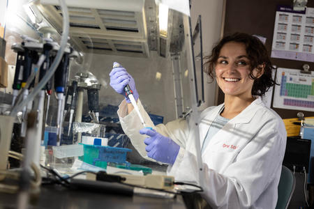 Sarah Aitken smiles while using a pipette under a hood