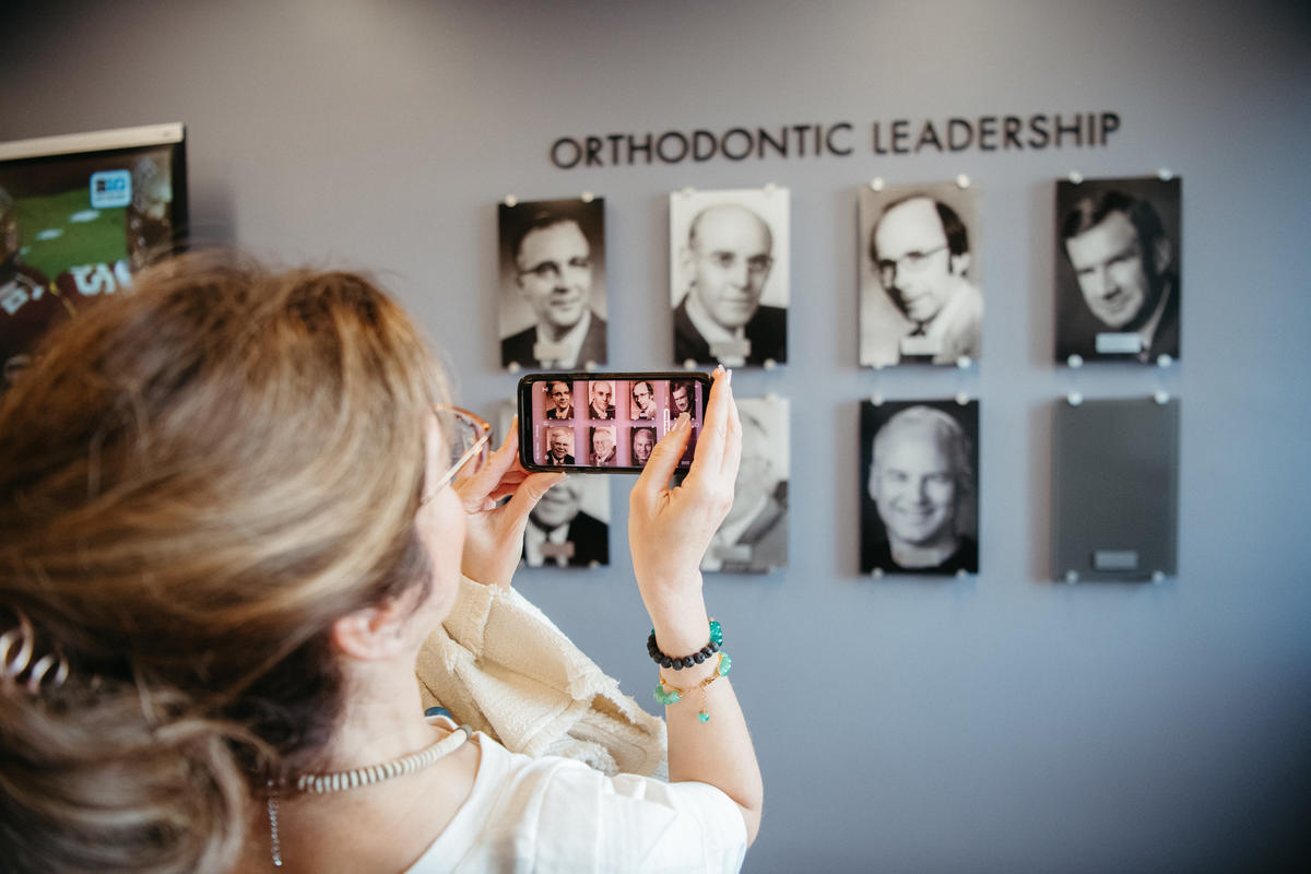 alumni attendee taking a smartphone picture of portraits of distinguished faculty on the wall in Moos Tower